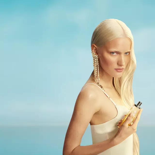 Nuevo banner de campaña de Mugler Starlicious les eaux gourmandes con una modelo con cabello rubio largo y ojos azules, con un vestido amarillo pálido, sosteniendo el frasco de la fragancia Pineapple Musk contra un fondo azul cielo suave. Las fragancias son deliciosas, coleccionables y combinables.