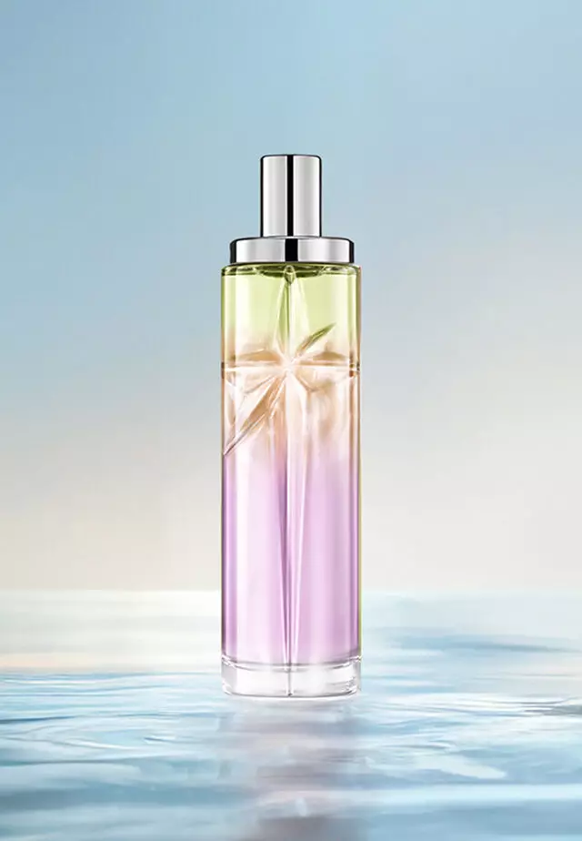 Receta de superposición de Sweet Kiss Starlicious: botella alta con degradado lavanda, ámbar y verde claro sobre agua y un fondo azul suave. Aroma afrutado y brillante con un toque gourmand; 3 pulverizaciones de Berry Licorice, 2 Pineapple Musk, 1 Pistachio Praline.