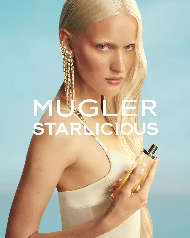 Banner de la campaña Mugler Starlicious Les Eaux Gourmandes con modelo en vestido amarillo pálido sosteniendo una botella de Pineapple Musk contra un cielo azul suave.