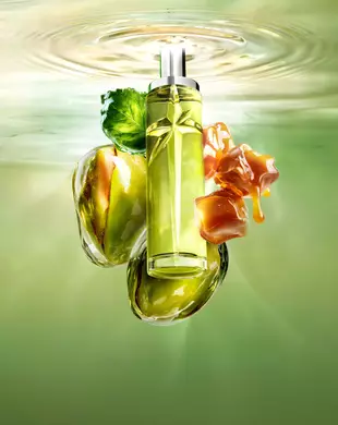 Nuevo Starlicious Pistachio Praline imagen de naturaleza muerta con el esbelto frasco rodeado de sus ingredientes clave: una hoja de pachulí, pistachos enteros y cubos de caramelo goteantes, todo sobre un fondo de agua ondulante verde luminoso.