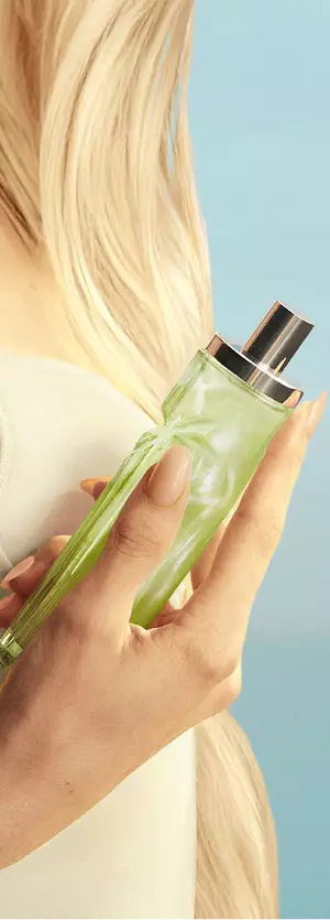 Nuevo recurso en mano de Starlicious Pistachio Praline con una modelo de pelo rubio largo y ojos azules, con un vestido amarillo pálido, sosteniendo el frasco de la fragancia pistachio praline