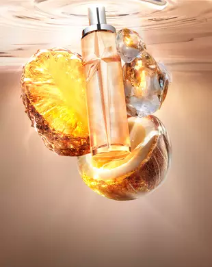 Nuevo Starlicious Pineapple Musk imagen de naturaleza muerta con el esbelto frasco rodeado de sus ingredientes clave: una rodaja de piña resplandeciente, una cáscara de coco agrietada y almizcle cristalino, todo sobre un fondo de agua ondulante cálido y luminoso.